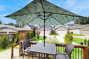 En terrasse med et bord og stole, en stor parasol og udsigt til et boligområde.