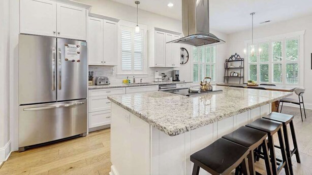 A modern kitchen with white cabinets, stainless steel appliances, a granite countertop island, and a large window with blinds. - Downtown Delight | Luxury home, walk to Main Street, bike to trails (Brevard)