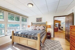 Ein Schlafzimmer mit Bett, Nachttischlampen, einem Fenster, einer Tür zu einer Küche und Blick ins Freie.