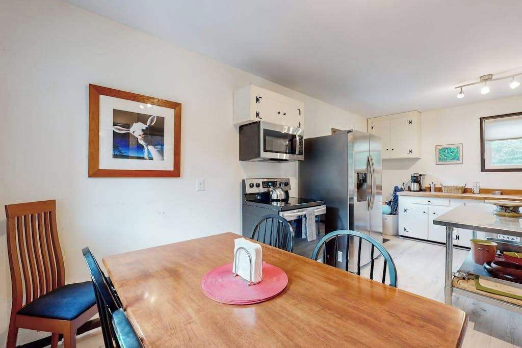 Une cuisine moderne avec des armoires blanches, un four à micro-ondes, une cuisinière et un réfrigérateur. On y trouve une table à manger avec des chaises et un tableau encadré accroché au mur.