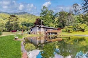 Ein Haus mit Terrasse, Teich und Bergen im Hintergrund.