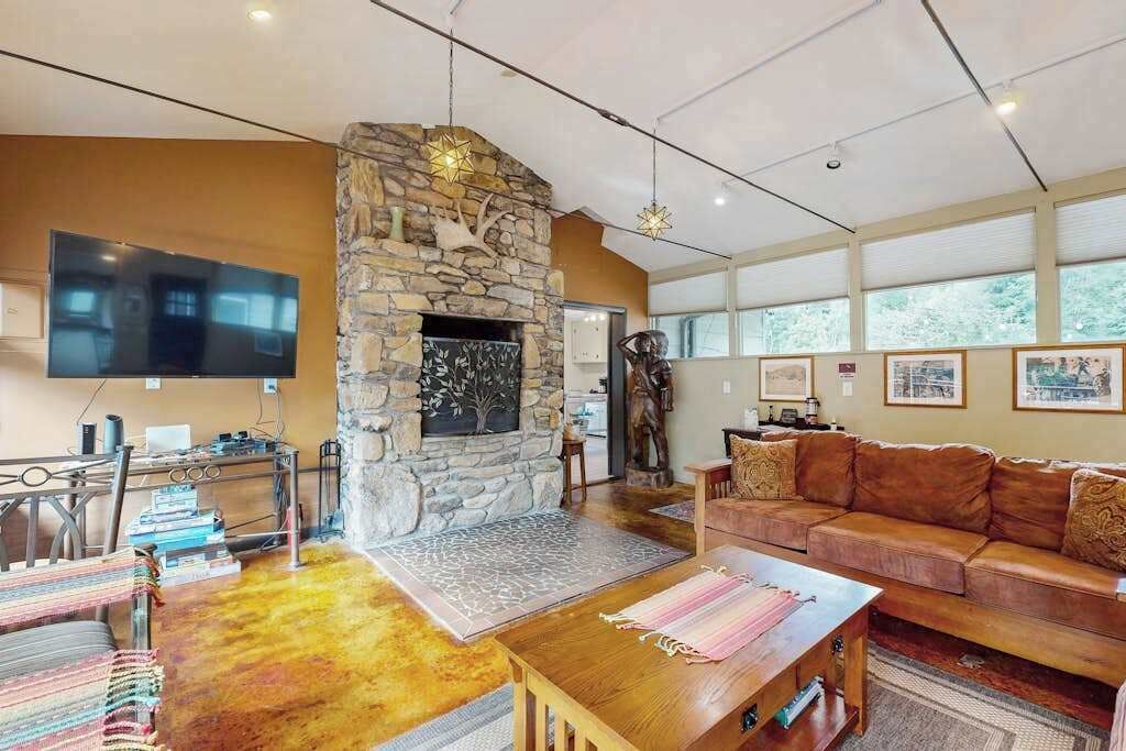 A living room with a stone fireplace, a flat-screen TV, a leather sofa, and artwork on the walls.