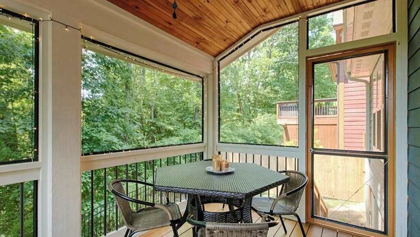 Un espace extérieur abrité, doté d’une table et de chaises, de grandes fenêtres et offrant une vue sur les arbres.