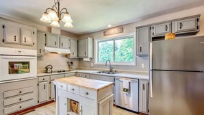 Una cocina con armarios grises, un refrigerador de acero inoxidable, una isla integrada con encimera de madera y un ventanal que proporciona luz natural.