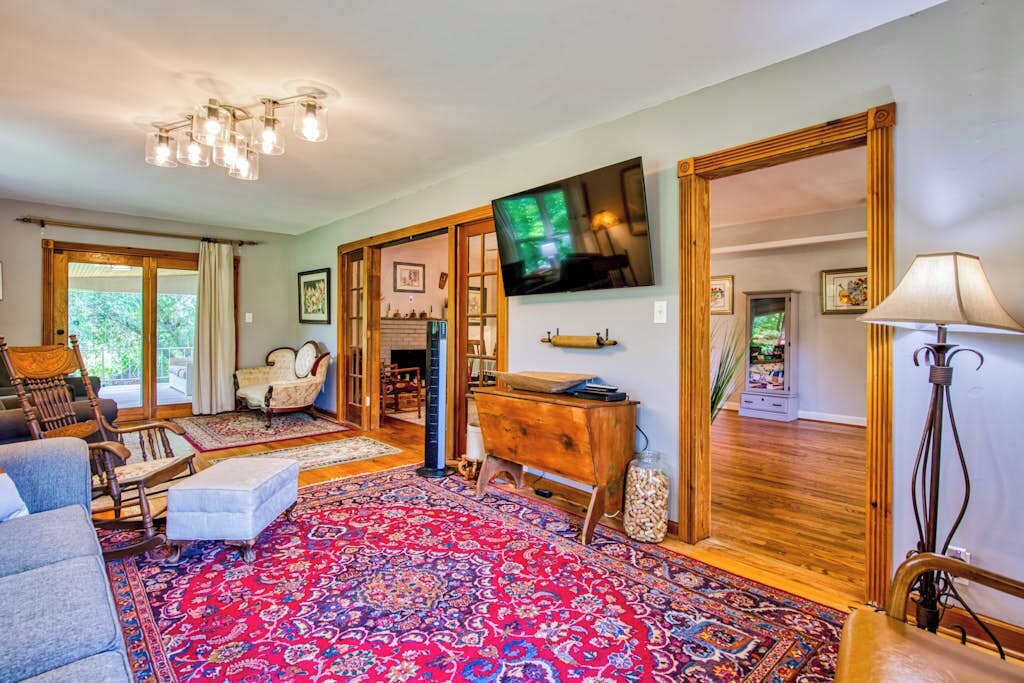 A spacious living room with a large red patterned rug, a television mounted on the wall, and a wooden cabinet.