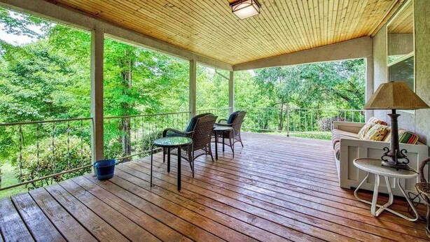 Un espacio al aire libre techado con suelo de madera, un sofá, dos sillones y una mesa.