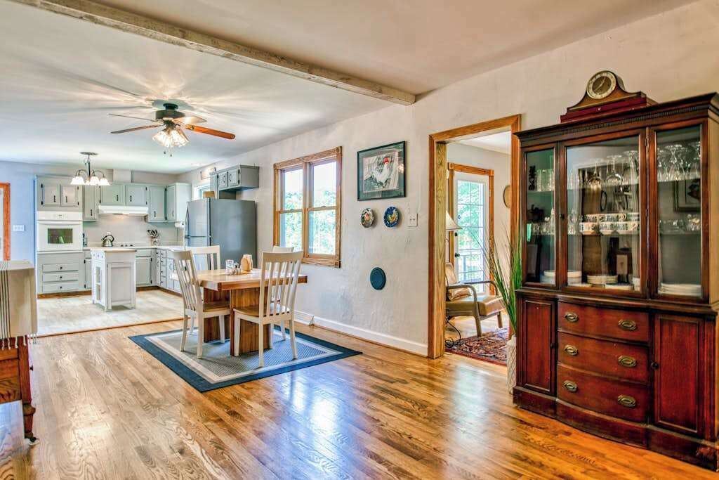 Une cuisine spacieuse avec un plancher en bois, un coin repas avec une table et des chaises, et un buffet traditionnel doté de portes en verre.