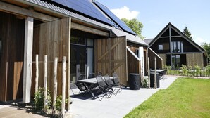 A building with a large solar panel roof, wooden exterior, and a patio with outdoor seating. - Lennepserf - De Hoeven (Veessen)