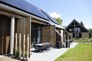 A building with a large solar panel roof, wooden exterior, and a patio with outdoor seating. - Lennepserf - De Hoeven (Veessen)