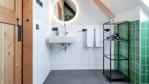 A modern bathroom with a wooden door, white tiled walls, a round mirror, a sink, and a shower area with green tiles. - Lennepserf - De Hoeven (Veessen)