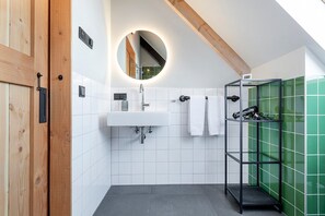 A modern bathroom with a wooden door, white tiled walls, a round mirror, a sink, and a shower area with green tiles. - Lennepserf - De Hoeven (Veessen)