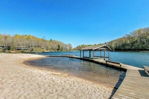 A sandy beach with a wooden dock extending into a calm body of water, surrounded by trees.