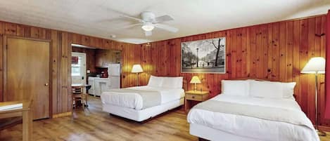 Ein Zimmer mit zwei Betten, Holzwänden, einem Deckenventilator und einem Essbereich, der durch eine offene Tür sichtbar ist.