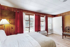 A hotel room with a bed, a chair, a window with curtains, and a door.