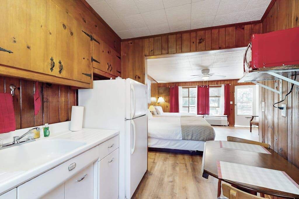 A room with wooden walls, a bed, a desk, and a window with curtains.