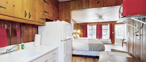 A room with wooden walls, a bed, a desk, and a window with curtains.