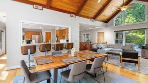 Un vaste espace de vie doté d’un plafond en bois, d’une table à manger avec des chaises, d’un canapé et offrant une vue sur l’extérieur.