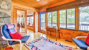 Ein Holzblockbau-Innenraum mit Steinwand, Deckenventilator, großen Fenstern und einer gemütlichen Sitzecke.