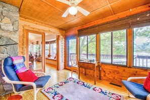Ein Holzblockbau-Innenraum mit Steinwand, Deckenventilator, großen Fenstern und einer gemütlichen Sitzecke.