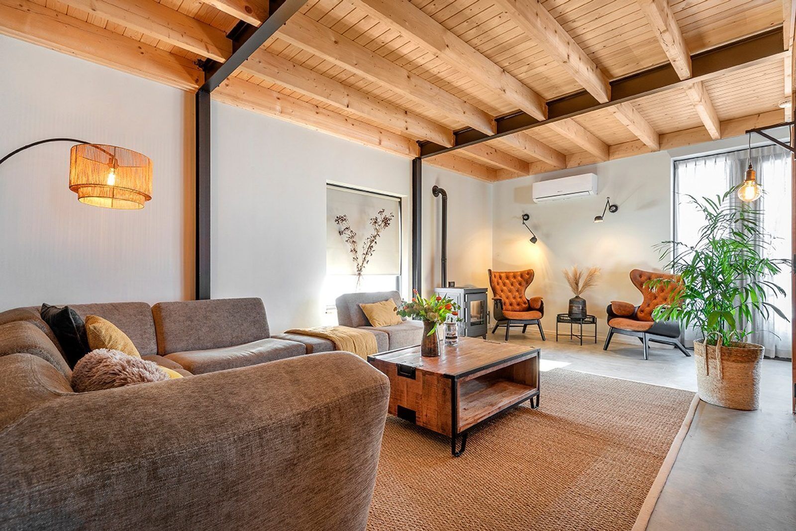 Un salon moderne avec un canapé, une table basse et deux fauteuils. On y trouve une cheminée, une plante et une grande fenêtre.