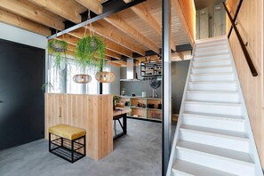 A modern interior with a wooden staircase, a dining area with a bench, and hanging plants. - Lennepserf - De Pinkels (Veessen)