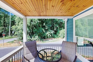 A covered porch with two chairs, a stop sign, and a view of a wooded area. - All-new cottage with deck, grill, & washer/dryer - near downtown & Rail Trail (Hendersonville)