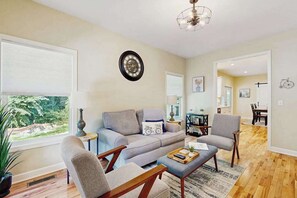 A living room with a sofa, armchairs, a coffee table, and a dining area with a table and chairs. - All-new cottage with deck, grill, & washer/dryer - near downtown & Rail Trail (Hendersonville)