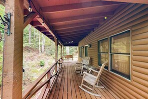 Eine Holzhütte mit verdeckter Veranda, Schaukelstühlen und großen Fenstern.