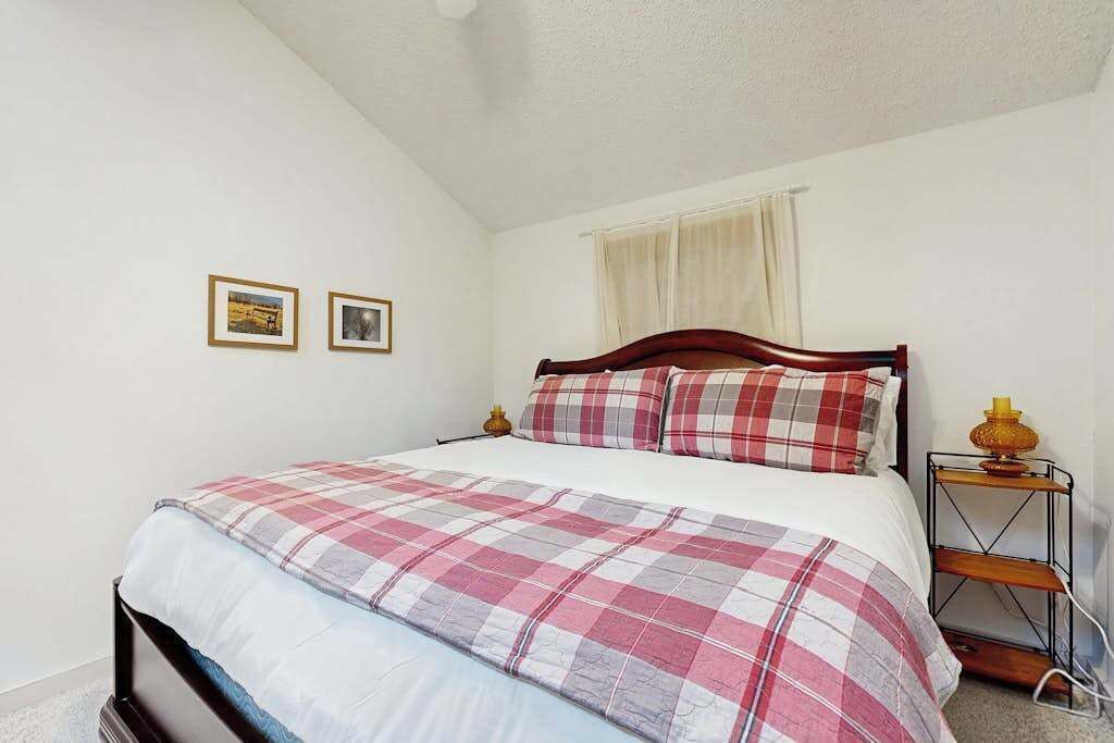 A bedroom with a bed, a bedside table, a lamp, and two framed pictures on the wall.