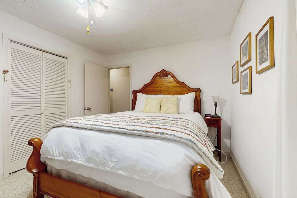 Une chambre à coucher avec un lit en bois, des murs blancs, une porte fermée et des tableaux encadrés accrochés au mur.