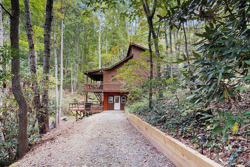 A rustic cabin with a porch, surrounded by a forest.