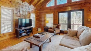 Interior de una cabaña de madera con televisión, sofá y mesa de centro.