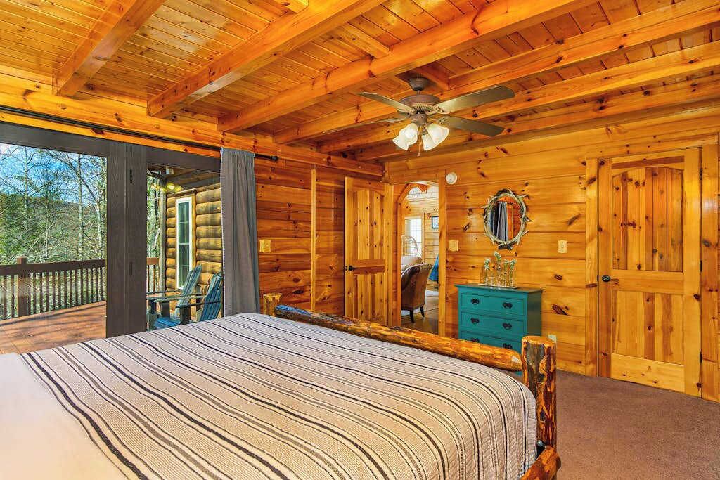 A log cabin bedroom with a bed, a dresser, a mirror, and a ceiling fan.