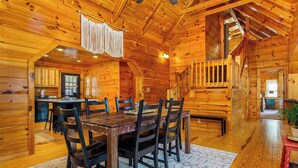 Interior de una cabaña de madera con comedor, cocina y una escalera.