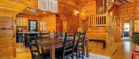Interior de una cabaña de madera con comedor, cocina y una escalera.
