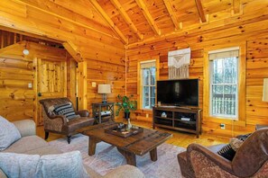 Ein Blockhaus-Interieur mit Holzbalkendecke, einem Fernseher, einem Sofa, einem Couchtisch und einem Fenster.