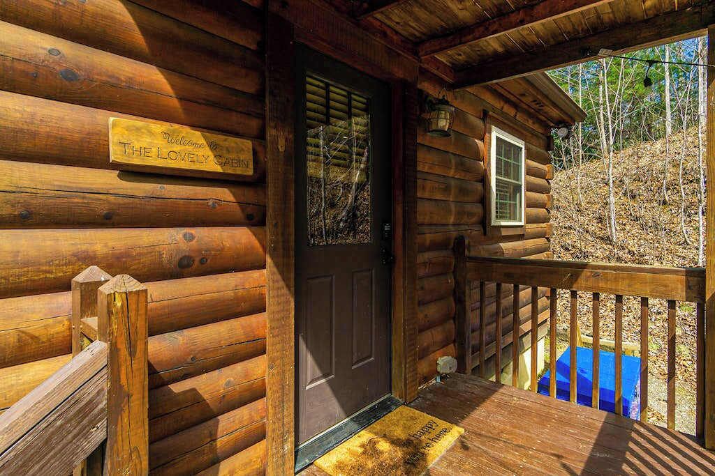 Una cabaña de madera con un letrero que dice 'Welcome to The Lovely Cabin', una puerta, una ventana y una terraza de madera.