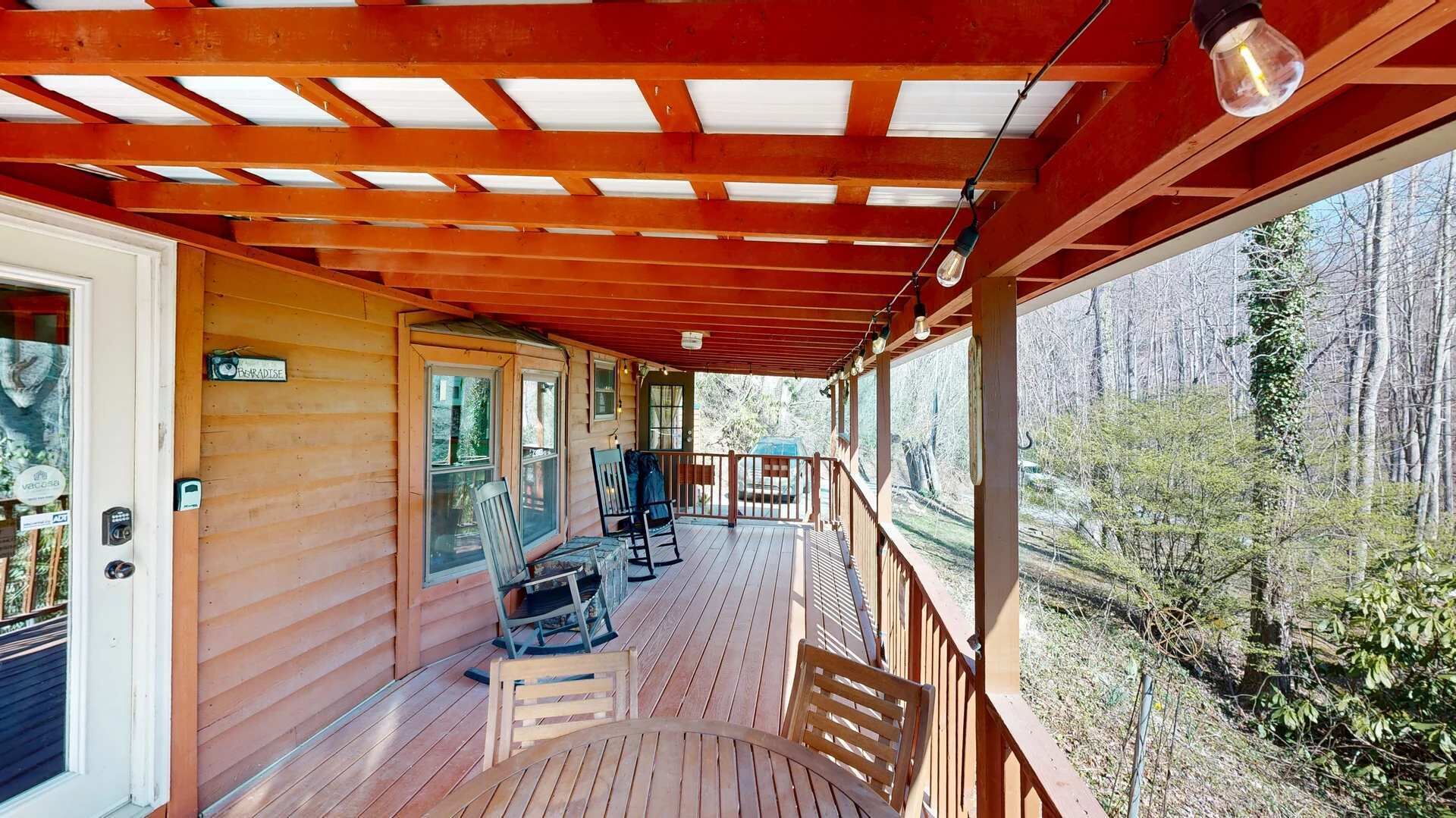 A wooden deck with a covered area, wooden railings, and a view of a forest.