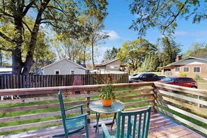 A wooden deck with a table and chairs, surrounded by a wooden fence, with houses and cars in the background. - Centrally located Brevard home - family friendly, perfect for outdoor adventures (Brevard)