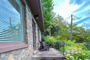 Ein Steinhaus mit Veranda, Bank und Garten mit Hortensien.