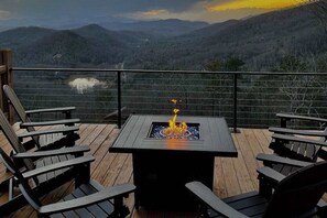 A deck with a fire feature, seating, and a view of a mountainous landscape. - Mountain view home with large deck, private hot tub and fire-pit (Fairview)