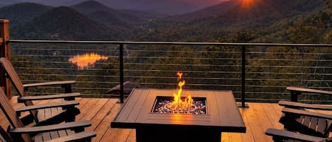 Terraza con fogón y sillas Adirondack con vista a un paisaje montañoso.