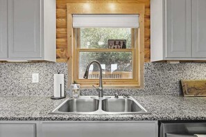 A kitchen with granite countertops, a double sink, and wooden cabinetry. - Mountain view home with large deck, private hot tub and fire-pit (Fairview)