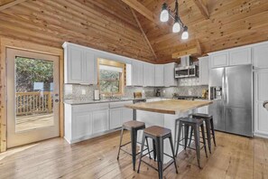 A kitchen with white cabinets, a wooden ceiling, and a stainless steel refrigerator. - Mountain view home with large deck, private hot tub and fire-pit (Fairview)