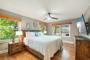 Ein Schlafzimmer mit Bett, Nachttischen, Deckenventilator, Fernseher und großen Fenstern mit Blick.