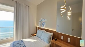 A hotel room with a bed, a nightstand, a mirror, and a view of the ocean.