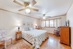 A bedroom with a bed, two nightstands, a chair, a rocking chair, a wooden cabinet, two ceiling fans, and a window with curtains. - Morris Villa Upper (Lake Junaluska)
