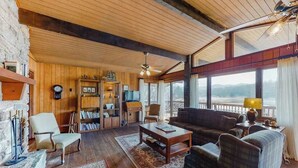 Un salón acogedor con chimenea, paredes de madera, un ventanal con vistas y un ventilador de techo.