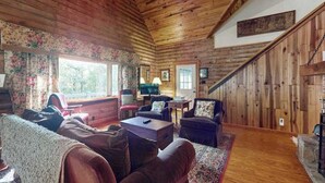 Interior acogedor de una cabaña con paredes de madera, chimenea, sofá y televisor.
