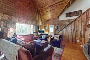 A cozy cabin interior with wooden walls, a fireplace, a sofa, and a television.